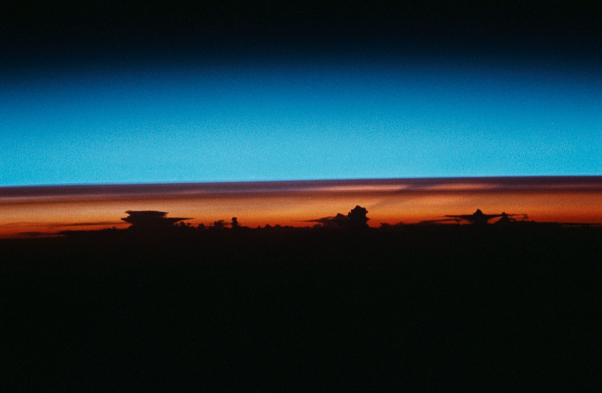 A glowing band of orange and blue — Earth's atmosphere at sunrise — arcing across the black of space, photographed from orbit.