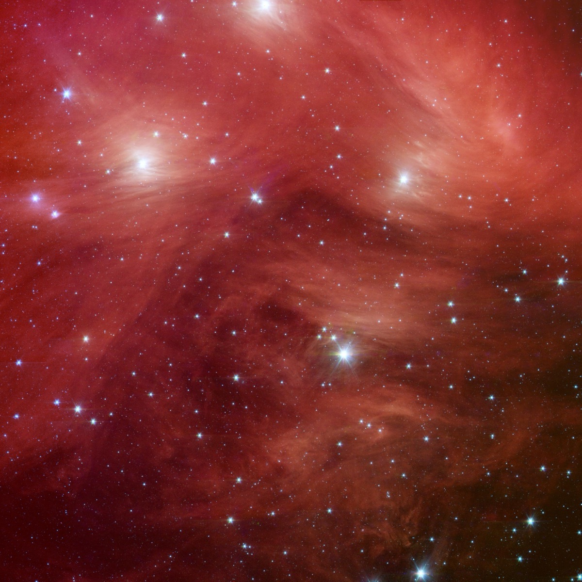 The Pleiades star cluster — a knot of bright blue-white stars wrapped in glowing pink and gold clouds of dust — in a Spitzer infrared image.